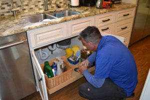 technician checking plumbing under kitchen sink
